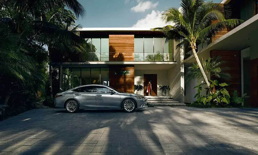 Srebrny Lexus przed nowoczesną willą z palmami.
